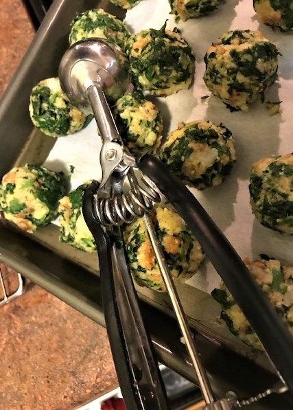 Spinach balls on tray showing ice cream scoop used to form balls.