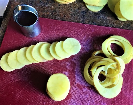 Picture of sliced potatoes and 1 1/2 inch cutter to make small disks for Cheesy Thyme and Ham Potato Gratin Stacks.