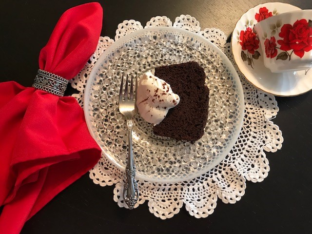 Slice of bittersweet chocolate quick bread with whipped cream on plate with teacup and fork.