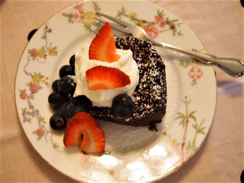 Single slice of wacky cake served with shipped cream and fresh blueberries and strawberries.